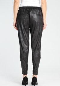 Svarta metalliska joggarbyxor med elastisk midja, avsmalnande ben och två bakfickor. Bärs med svarta högklackade skor.