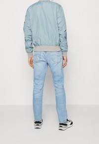 Light blue bomber jacket with a ribbed gray hem, paired with light blue jeans and black sneakers, showing a relaxed fit and casual style.