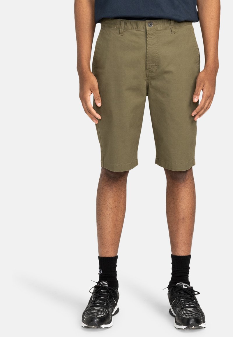 Olivgröna shorts med slät front, knappstängning och bälteshällor. Bärs med svarta sneakers och strumpor. Slät tygstruktur.