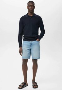 Suéter de punto azul marino, pantalones cortos de mezclilla y sandalias negras. El suéter tiene un cuello clásico, mientras que los pantalones cortos son de color azul claro y tienen un estilo casual.