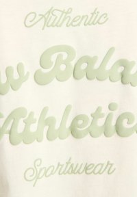 Crème-kleurige stof met verhoogde lichtgroene tekst waarin "Authentiek," "Balanco," "Athletisch," en "Sportkleding" staat.
