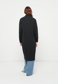 Un long cardigan gris foncé en matière tricotée douce, doté d'un col châle et de poignets côtelés, s'étendant jusqu'à mi-mollet.