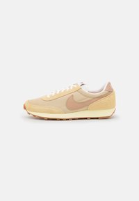 Beige retro sneakers with mesh and suede materials, white laces, and a tan Nike swoosh. Light-colored sole with a textured tread pattern.