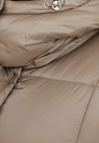 Beige pufjakke med en blank finish, der har en høj krave, knaplukning og syede paneler til isolering.