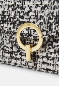 Sac en tweed noir et blanc avec un tissu texturé, doté d'un fermoir circulaire doré et d'une gravure de la marque. Motif distinctif et accents métalliques.