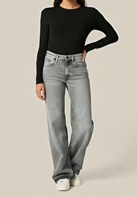 Černý top s dlouhým rukávem v kombinaci s vysokým pasem, světle šedými širokými džínami. Džíny mají klasický design s pěti kapsami a jemně vybledlou texturu.