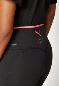 Svarta högmidjade leggings med rosa detaljer, prydda med en Puma-logotyp. Tillverkade av ett elastiskt material med en slät textur och detaljerad sömnad.