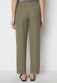 Olijfgroene, losvallende broek met een elastische tailleband, rechte pijpen en een enkele achterzak. De stof heeft een zachte, lichte glans.