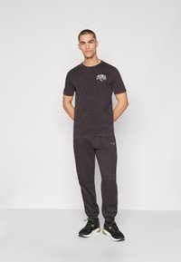 Black T-shirt with a faded texture and white Puma logo, paired with dark sweatpants and black sneakers with green accents.