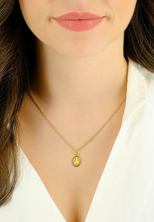 Collier en or avec un pendentif ovale texturé présentant des détails intriqués, porté au-dessus d'un vêtement à col blanc.