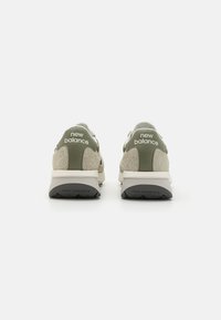 Zelena i bež tenisice s teksturiranim gornjim dijelom, podstavljenim ovratnikom i bijelim međuslojom, s "New Balance" oznakom na peti.