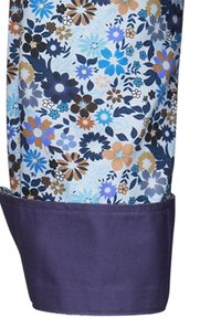 Tessuto con motivo floreale che presenta fiori blu, marroni e arancioni su uno sfondo chiaro, con un polsino viola scuro nella parte inferiore.
