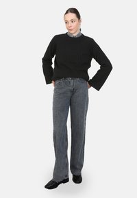 Schwarzer gerippter Pullover mit langen Ärmeln, kombiniert mit hoch taillierten grauen Jeans und schwarzen Schuhen, im entspannten Schnitt.