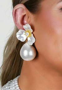 Blommörhängen med en vit kronbladsdesign, central pärla och guldaccenter, samt en stor, slät, metallisk hängande pärla.