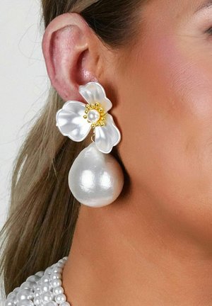 Blumenohrringe mit einem weißen Blütenblatt-Design, das eine zentrale Perle und goldene Akzente aufweist, kombiniert mit einem großen, glatten, metallic aussehenden Perlenanhänger.