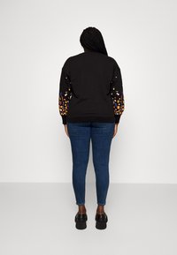 Black sweatshirt with colorful floral embroidery on puffed sleeves, paired with blue skinny jeans and black platform shoes.