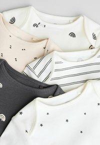 Quatre débardeurs pour bébé, présentant divers motifs : un avec des motifs arc-en-ciel, un avec des pois, un avec des rayures noires, et un orné d'étoiles.