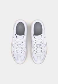 Chaussures de sport blanches avec une tige en cuir lisse, des accents texturés, des lacets ronds et une semelle en caoutchouc de couleur claire. Semelle intérieure Ortholite visible.