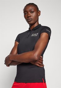 Μαύρο polo μπλουζάκι κατασκευασμένο από υφασμάτινη ύλη με υφή, διαθέτει κλείσιμο με κουμπιά στον γιακά και κοντά μανίκια. Λογότυπο στο στήθος και "VENTUS" στο μανίκι.