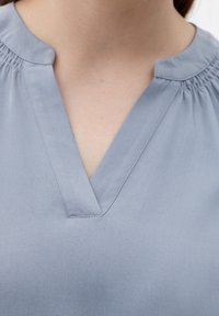 Helles blaues V-Ausschnitt-Bluse mit Raffung am Ausschnitt. Aus glattem Stoff mit leicht strukturiertem Finish.