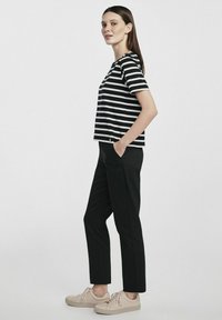 Czarny i biały T-shirt w paski o luźnym kroju, zestawiony z czarnymi spodniami prostymi i beżowymi tenisówkami. Prosty, casualowy design.