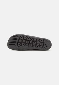 Black rubber shoe sole with circular grip patterns and textured detailing, featuring elongated grooves and branding.