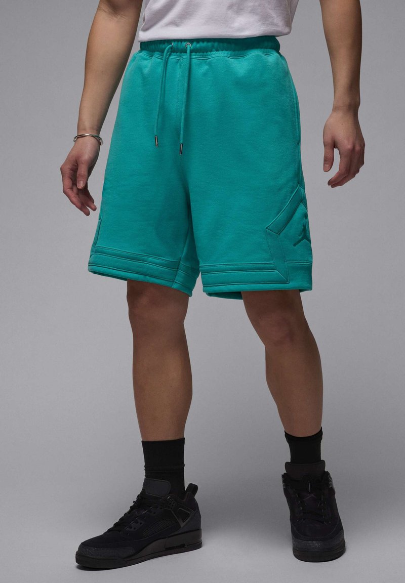 Tyrkise sweat shorts med snor i taljen, sidelomme og ribbet kantdetalje. Båret med sorte sneakers og strømper.