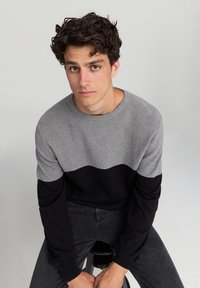 Szary i czarny sweter z karbowaną fakturą, z falistym kontrastowym wzorem. Okrągły dekolt i długie czarne rękawy.