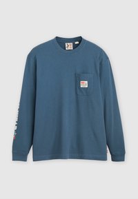 Blaues Langarm-T-Shirt aus Baumwolle mit einer Brusttasche, die ein Etikett und bedruckten Text entlang des linken Ärmels hat. Klassischer Rundhalsausschnitt.
