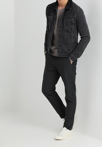 Chaqueta de mezclilla negra para hombre con un cuello en contraste, suéter gris y pantalones jogger oscuros. El conjunto incluye zapatillas blancas, con líneas y texturas limpias.