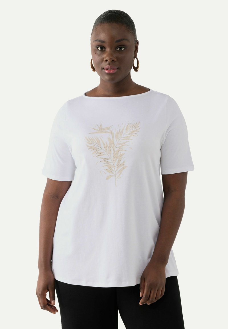 Camiseta de algodón blanca con un estampado de helecho dorado en el centro. La camiseta tiene mangas cortas y un escote redondeado, combinada con pantalones negros.