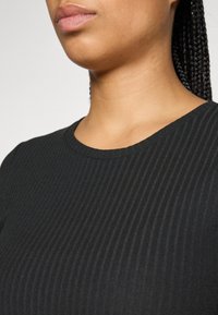 Black ribbed top featuring a round neckline, close-fitting design, and textured fabric. The neckline is smooth and finishes at the collarbone.