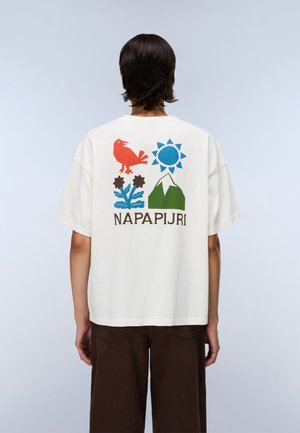 Personne portant un t-shirt blanc avec des graphismes colorés d'oiseau, fleur, soleil, montagne, et le texte "NAPAPIJRI" dans le dos, debout devant un fond clair.