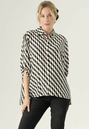 Black and white button-up blouse with a wave pattern, lightweight fabric, roll-up sleeves, and a loose fit. Worn with black skinny jeans.