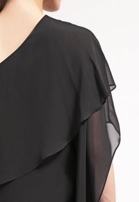 Czarny top z szyfonu z warstwowym, zwiewnym materiałem, z dekoltem w kształcie litery V z tyłu oraz przezroczystą teksturą przy rękawach.