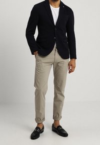 Blazer blu navy con revers a gola, t-shirt bianca, pantaloni chino beige e mocassini neri. Il blazer presenta due tasche frontali e una chiusura con bottone.