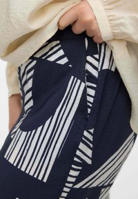 Tessuto blu navy con audaci motivi geometrici bianchi. Primo piano di una vita elasticizzata con pieghe visibili e dettagli di texture.