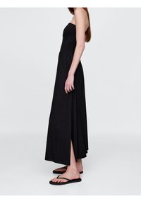 Svart axelbandslös maxiklänning med en figurnära bodice, fladdrande kjol och en sidoflik, kombinerad med svarta flip-flops. Slät tyg, enkel design.