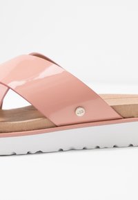 Roze verende sandaal met een brede kruisstrop, een gestructureerde binnenzool, een witte zool en een gouden logoaccent. Gladde en glanzende afwerking.
