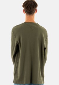 Camisa térmica de manga larga en color verde oliva con un patrón de canalé texturizado, cuello redondo y corte relajado. Presenta un sutil detalle de costura en la parte posterior.