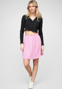 Čierny rebrovaný crop top s gombíkmi; svetloružová sukňa s elastickým pásom; biele tenisky; hladká textúra, neformálny štýl a uvoľnený strih.
