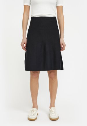 A knee-length black skirt made of a textured fabric, featuring a flared design and a fitted waist, paired with white sneakers.