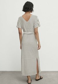 Randig maxiklänning med korta, vida ärmar och V-formad rygg. Tillverkad av mjukt tyg, med en sidoklyfta och knytmidja. Färg: kräm- och svartrandig.