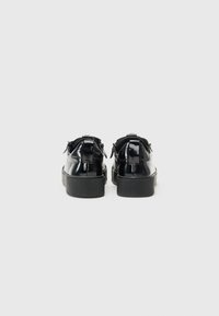 Scarpe in pelle verniciata nera con una texture liscia, punta arrotondata e suola in gomma bassa. Presentano cuciture sottili e un'anello posteriore per indossarle facilmente.