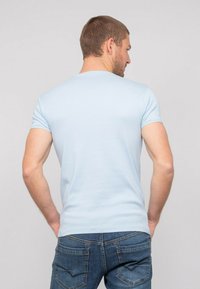 T-shirt bleu clair à manches courtes au design ajusté, fabriqué en tissu doux, avec un col rond et une texture lisse, associé à un jean.