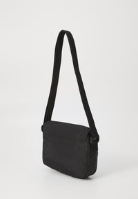 Borsa a spalla nera realizzata in tessuto morbido, forma rettangolare, tracolla regolabile, chiusura a patta e design minimalista senza hardware visibile.