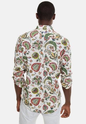 Mann trägt ein weißes Langarmhemd mit mehrfarbigem Paisley-Blumenmuster, hochgekrempelte Ärmel, kombiniert mit weißer Hose, von hinten gesehen.