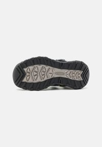 Sole di scarpe da trekking nere con scanalature profonde, dotata di una intersuola grigia e di un design a motivi per trazione e durata.