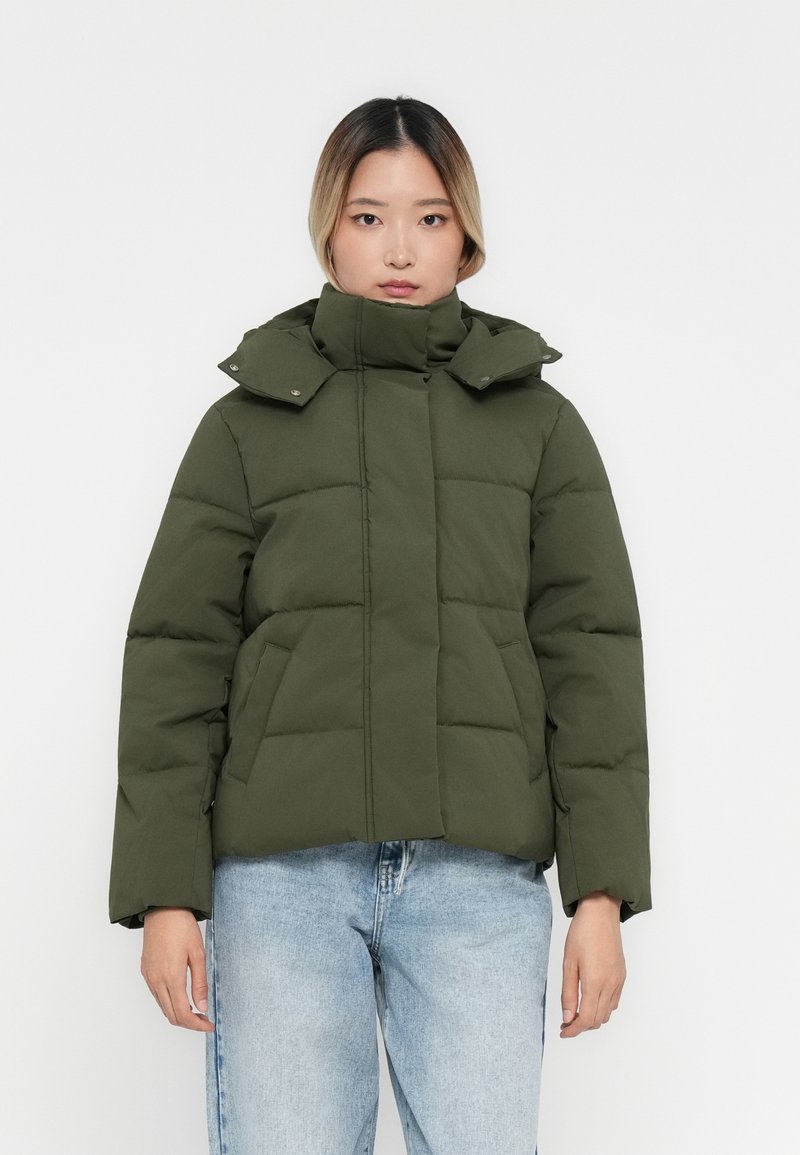 Chaqueta acolchada verde oscuro con un alto cuello, botones a presión y bolsillos laterales. Presenta una forma cuadrada y una textura suave.