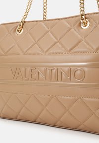 Tan kviltad läderhandväska med en deprimerad "Valentino"-logotyp, guldtonade kedjesträngar och diamantmönstrad textur genom hela väskan.